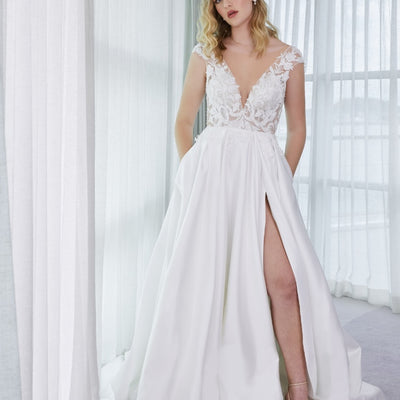 Tianna gown with full A-line skirt with pleated detail opening to dramatic split. Bodice is beaded with lace with plunging v-neckline. Lace drips down from bodice and decorates top of skirt. Small capped sleeves of beaded lace.