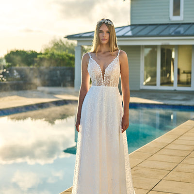 Penelope gown with plunging v-neckline framed by beaded daisies. A soft A-line skirt joins at the waist. Beaded leaf detailing covers the entire gown. A structured hem creates a ripple effect.