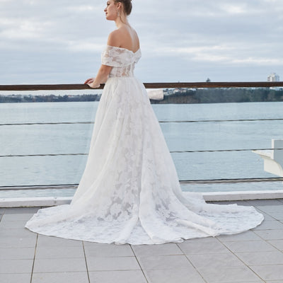 Back view of Teresa. Sheer floral organza with ivory lining in skirt and visible ivory boning through the bodice. Off shoulder sleeve band meets at centre back.