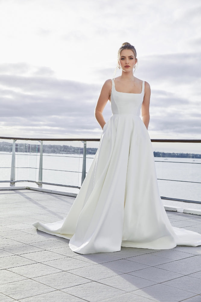Minimalist ivory satin a-line gown with square neckline. Trinity has a dramatic skirt with pockets.