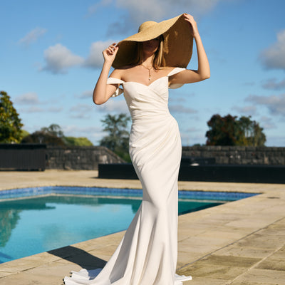 Priscilla gown in ivory crepe. Ruched crossover fit-n-flare silhouette with off-shoulder draped straps.