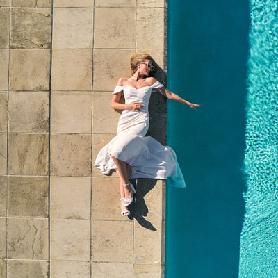 Birds eye view of model wearing priscilla dress laying by pool. Sweetheart neckline, ruching detail through bodice.