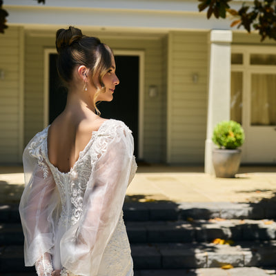 Back of the bodice in shallow scoop shape. Adorned with lace motifs. Sheer balloon sleeves with lace cuffs.